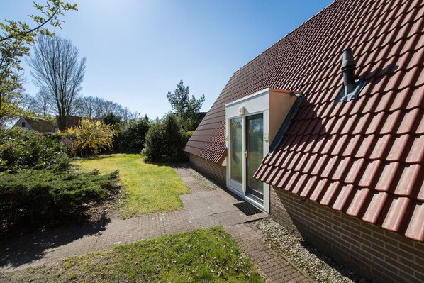 A house with a red-tiled roof, a brick exterior, and a small garden with a pathway leading to a door.
