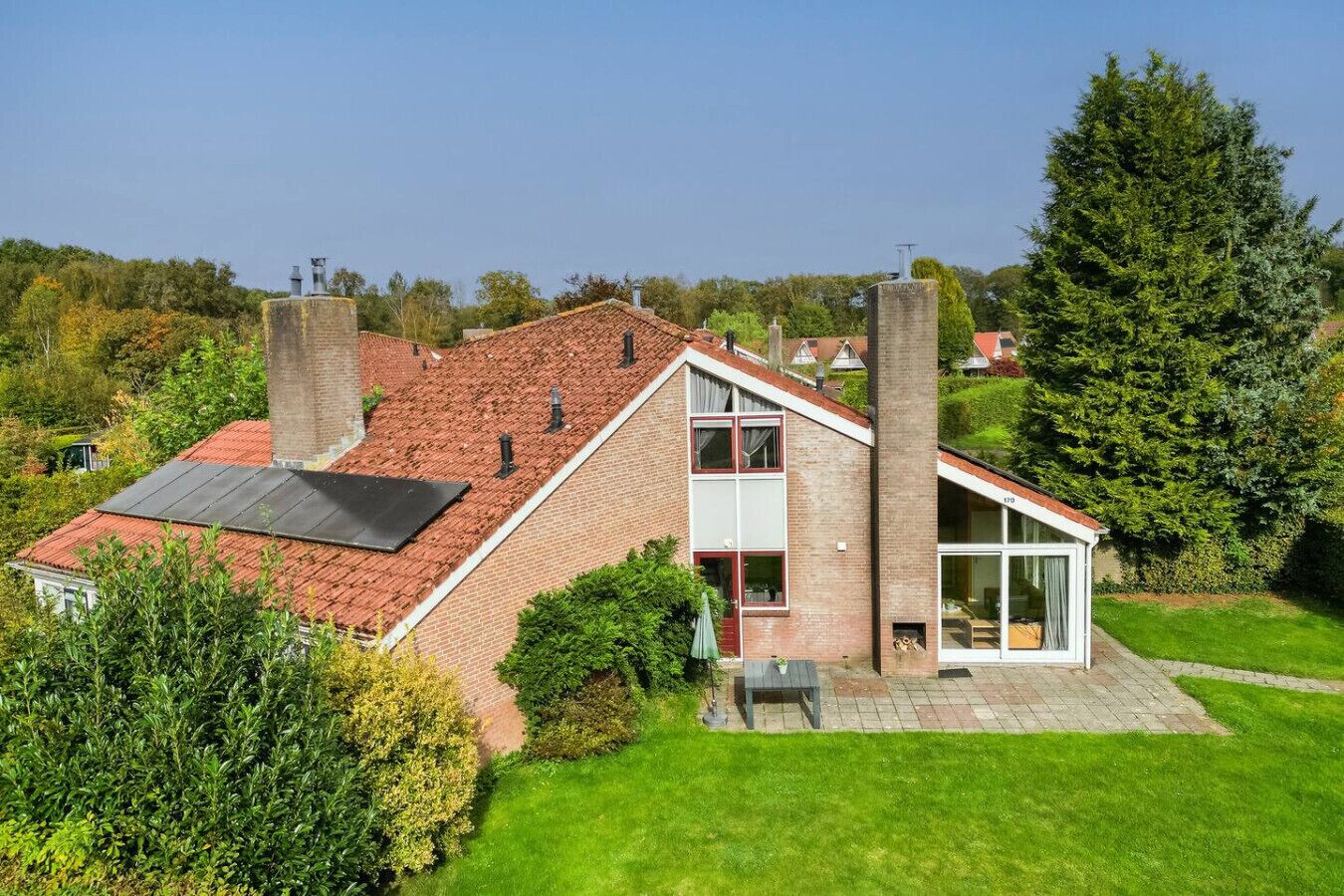 Een huis met twee verdiepingen, een schuin dak, een bakstenen schoorsteen en een glazen conservatorium.