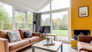 Ein modernes Wohnzimmer mit einer Couch, einem Couchtisch und einem Fernseher, großen Fenstern und einem Kamin.