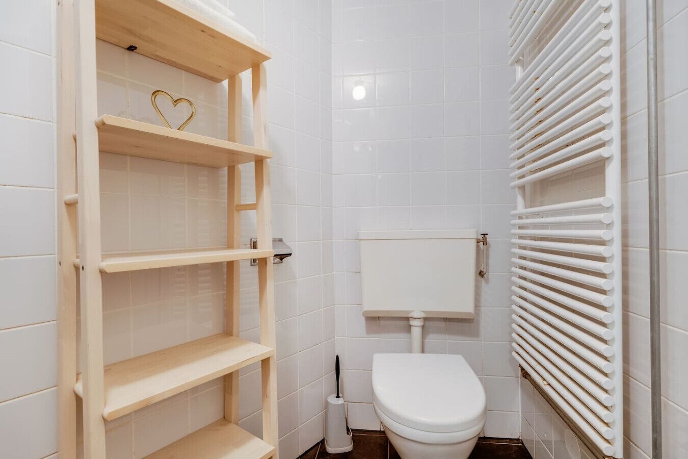 Een badkamer met witte betegelde wanden, een toilet, een houten plank en een radiator.
