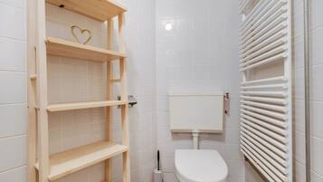 Een badkamer met witte betegelde wanden, een toilet, een houten plank en een radiator.