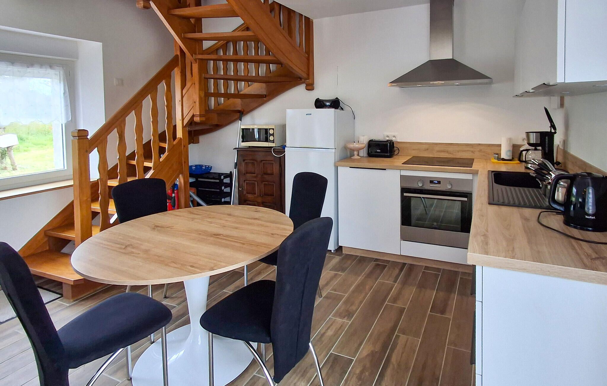 A modern kitchen with a wooden staircase, a round dining table with chairs, a built-in oven, and a coffee machine.