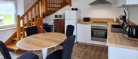 A modern kitchen with a wooden staircase, a round dining table with chairs, a built-in oven, and a coffee machine.