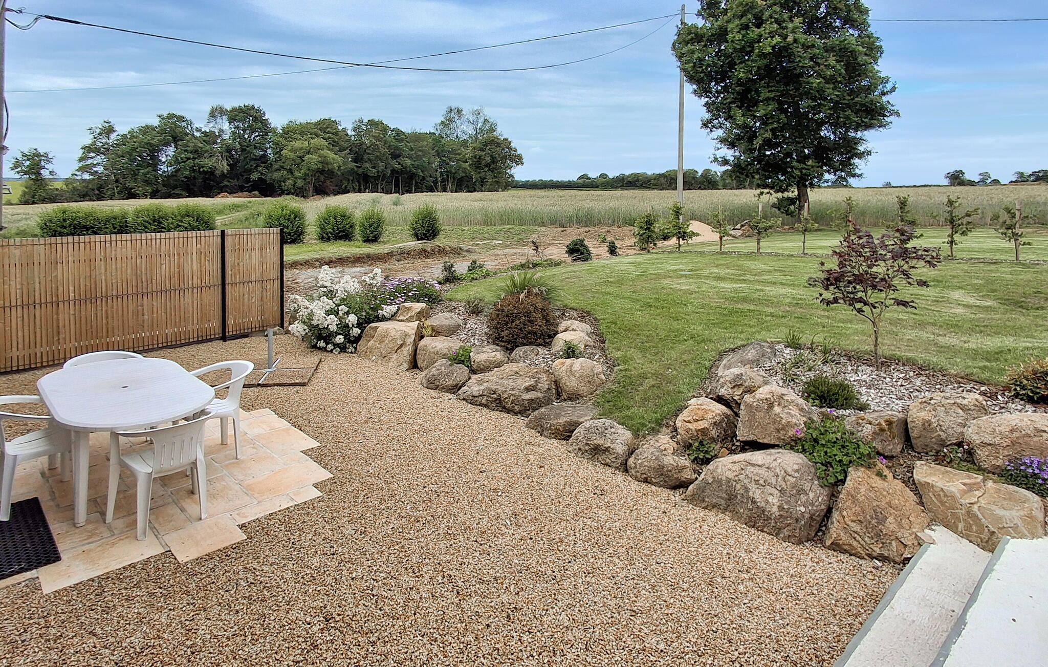 Um pátio com mesa e cadeiras, rodeado por um jardim com pedras e plantas.