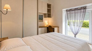 Ein Schlafzimmer mit Bett, Schreibtisch, Stuhl, Lampe und einem Fenster mit Vorhang.