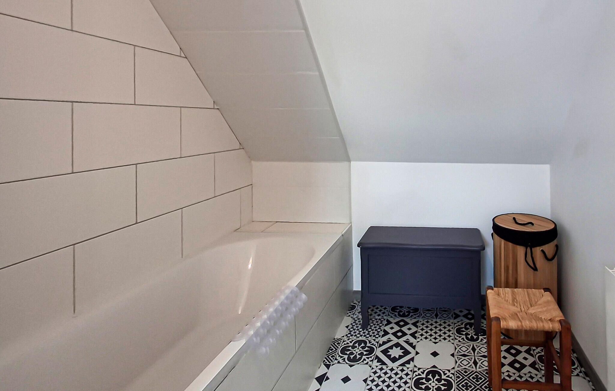 Une salle de bain avec une baignoire, une poubelle et un tabouret en bois.