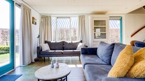 A modern living room with a grey sofa, a round coffee table, and a large window with curtains. - Fieldfare I Home with Fine Garden (Zwiggelte)