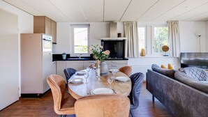 A modern kitchen with a dining area, featuring a large table set for four, a sofa, and a TV. - Fieldfare I Home with Fine Garden (Zwiggelte)