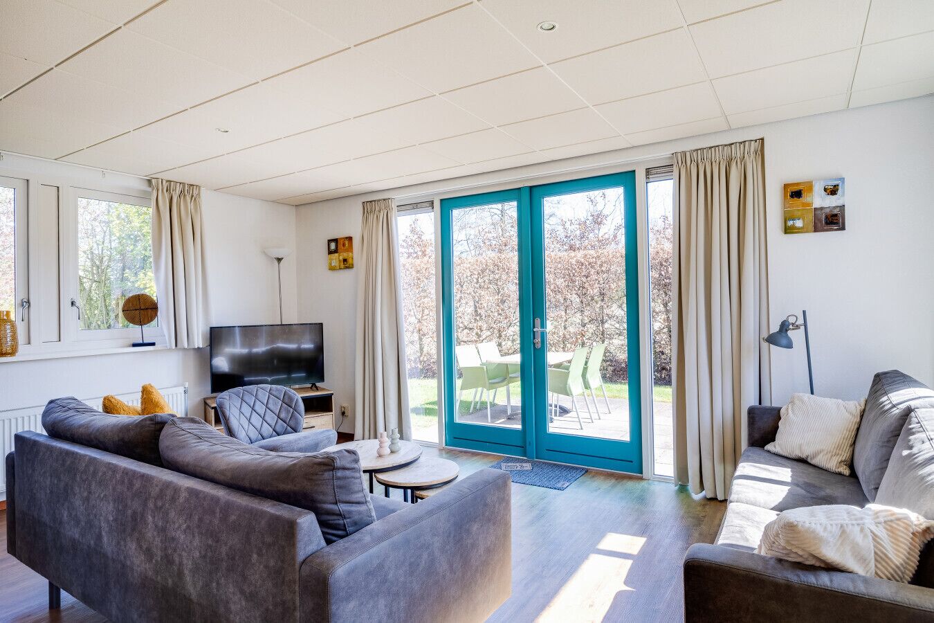 A modern living room with a sofa set, a flat-screen TV, and a dining area with chairs. - Fieldfare I Home with Fine Garden (Zwiggelte)