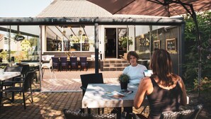 Een terras met tafels en stoelen, een overdekte patio en een gebouwde ingang met een 'Welcome' bord.