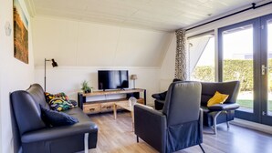 Een moderne woonkamer met een flatscreen televisie, twee zwarte leren banken, een houten salontafel en een grote glazen schuindeur die leidt naar een tuin.