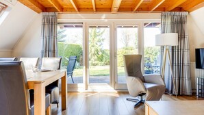 A modern, well-lit room with a wooden ceiling, a dining area with a table and chairs, a large window with curtains, and a television. - Lovely House I View Garden and Farmland (Zwiggelte)