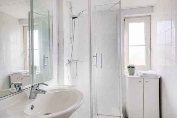 A modern bathroom with a white sink, a glass shower enclosure, and a window with a view.