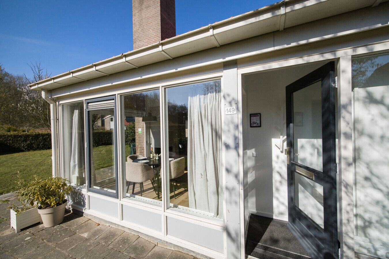 Een modern huis met een tuinkamer, grote glazen deuren, een bakstenen schoorsteen en een verzorgde tuin.