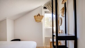 Ein Schlafzimmer mit einem Bett, einem Holzstuhl, einem Schreibtisch und einem Fenster mit Vorhängen.