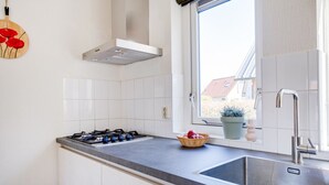 A modern kitchen with white cabinets, a gas stove, a stainless steel sink, and a window with a view of a house. - Cuckoo I Modern Home with Private Garden (Zwiggelte)