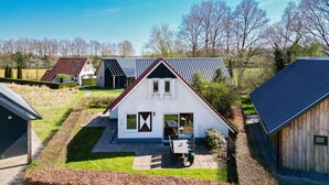 A white house with a red roof and a small patio with a table and chairs. - Cuckoo I Modern Home with Private Garden (Zwiggelte)