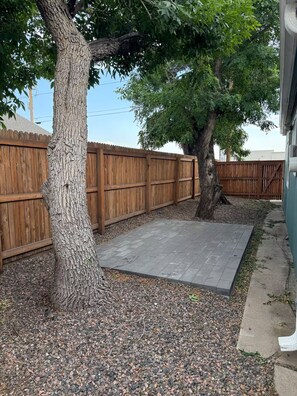 A backyard with a wooden fence, a tree, and a paved patio area. - 3BR Denver Home with Yard & Gated Parking (Denver)
