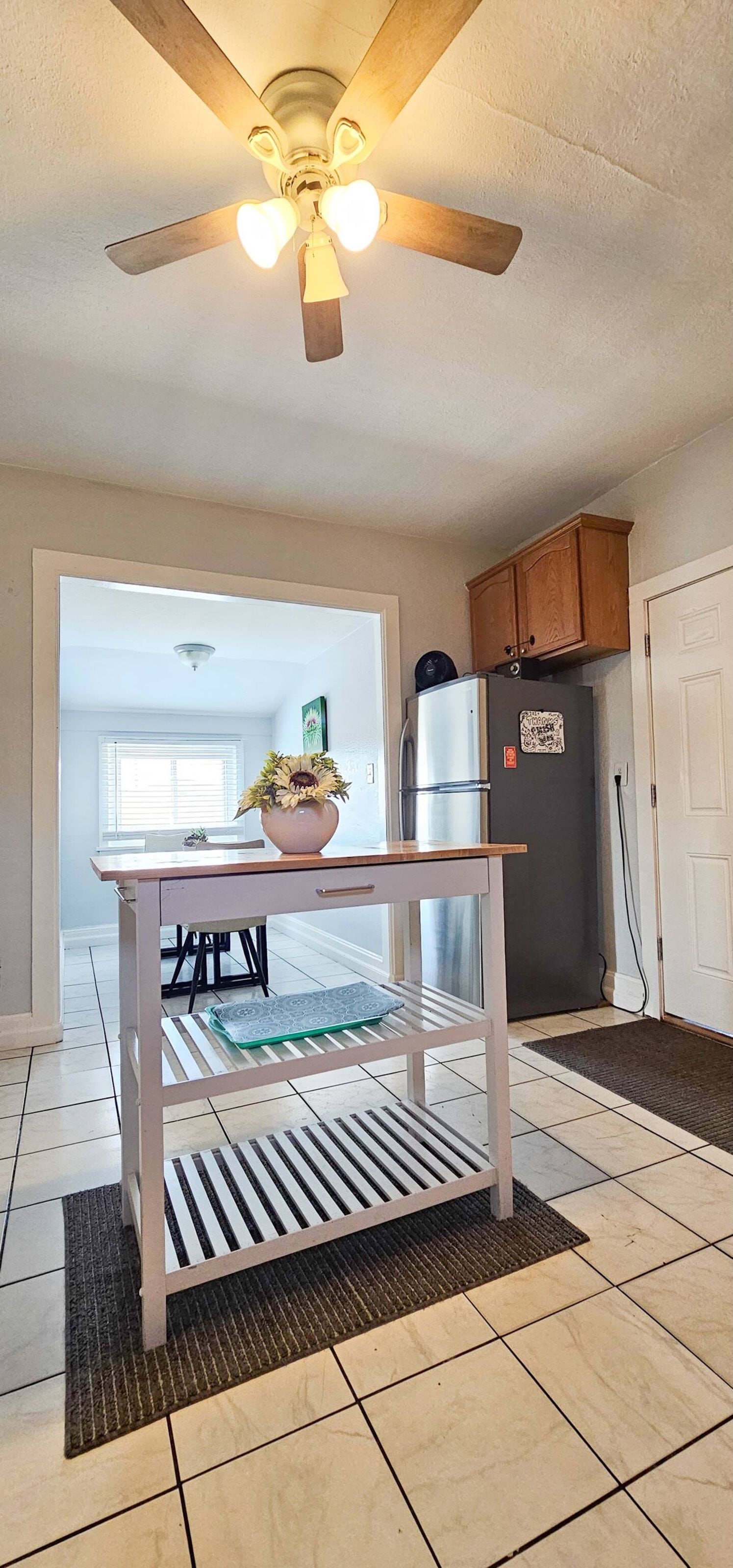 Una cocina con ventilador de techo, refrigerador y una mesa de comedor con sillas.