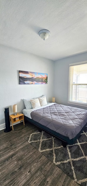 A bedroom with a bed, a nightstand, a lamp, a painting, and a window. - 3BR Denver Home with Yard & Gated Parking (Denver)