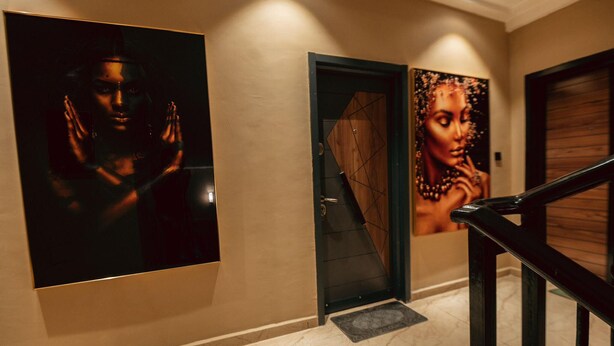 Un corridoio con pavimento in marmo, una porta in legno e due grandi opere d'arte incorniciate al muro.