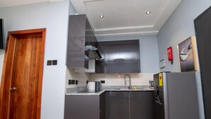 Una cucina moderna con mobili scuri, una porta in legno, una cappa aspirante in acciaio inossidabile, un frigorifero e uno schienale rivestito di piastrelle.