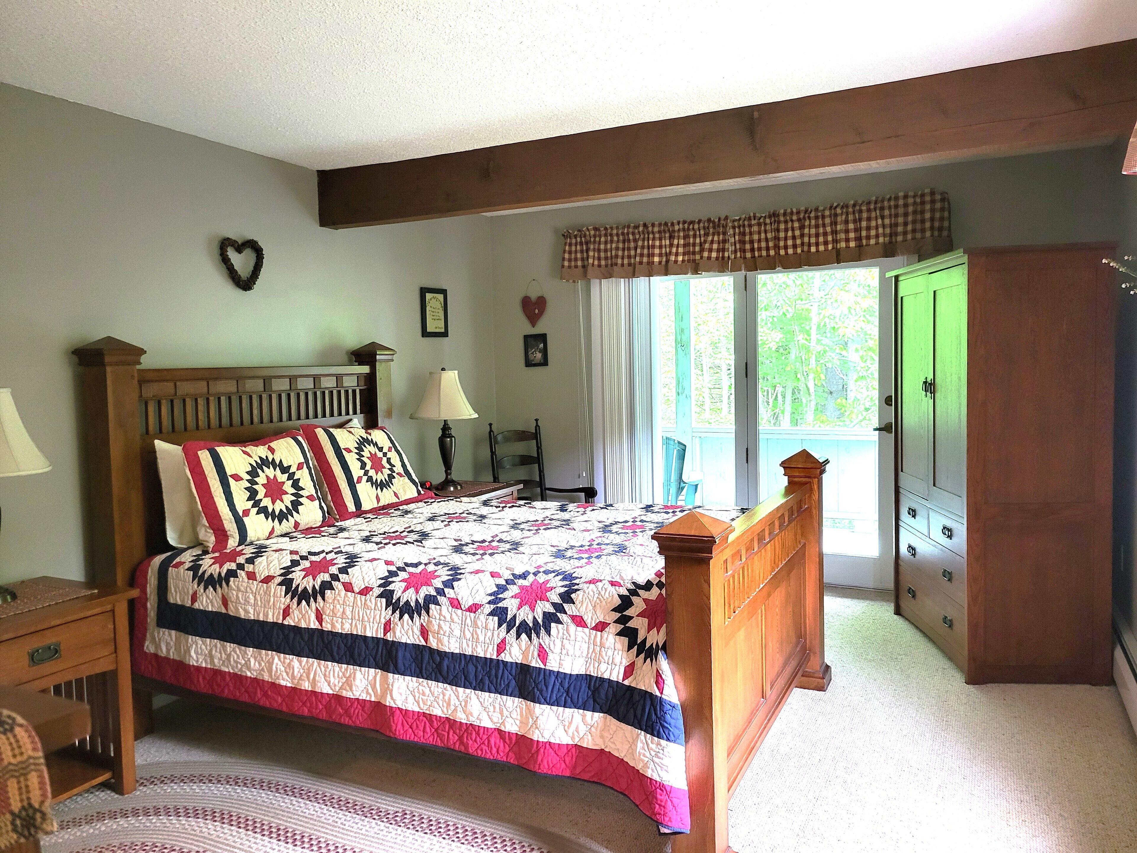 Un dormitorio con cama de madera, una mesita de noche, una silla, una ventana con cortinas y una puerta verde.