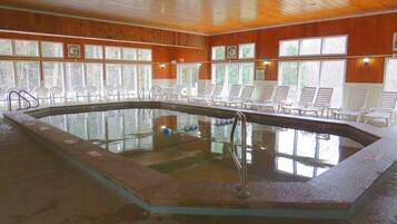 Una piscina interior con revestimiento de madera, rodeada de sillones de descanso y grandes ventanales.