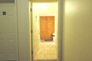 En hall som leder till ett rum med en trädörr, en papperskorg och en matta på golvet.