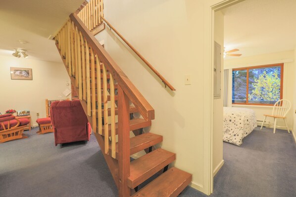 A wooden staircase leading to a second floor, carpeted floors, a window with a view, and a red chair in the room.