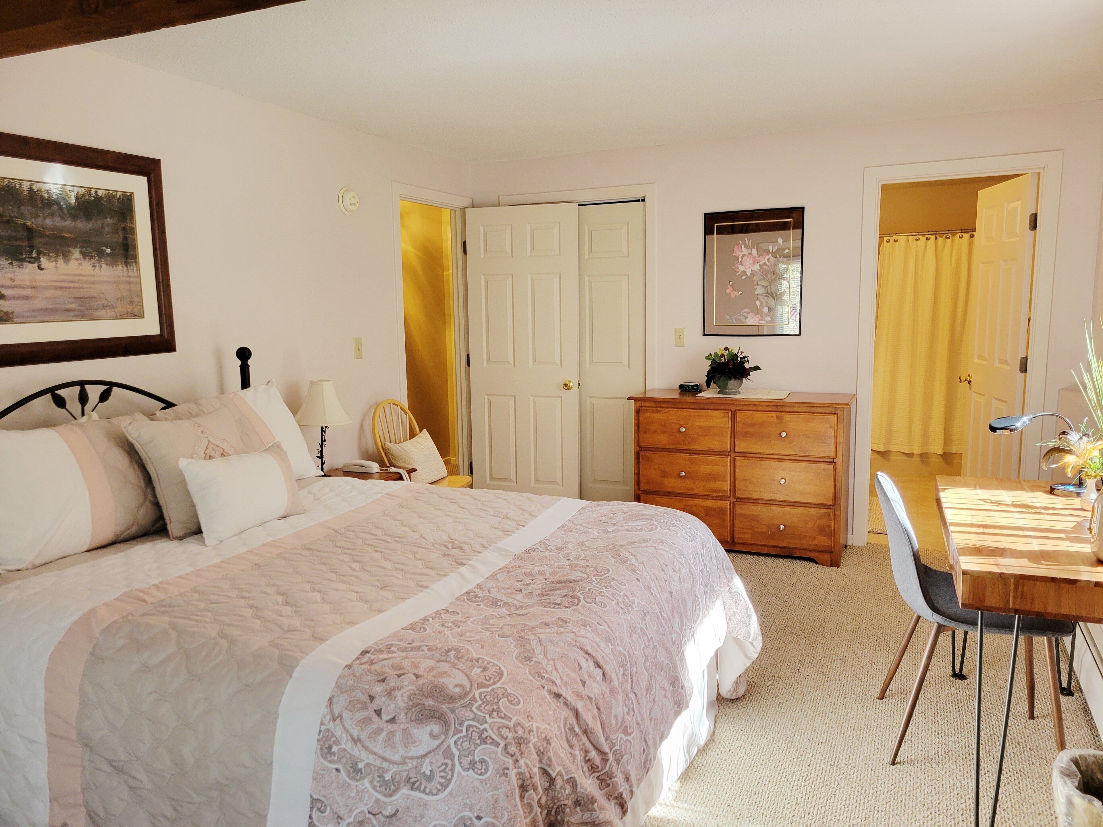 Ein Schlafzimmer mit Bett, Kommode, Stuhl, Schreibtisch und einer Tür.