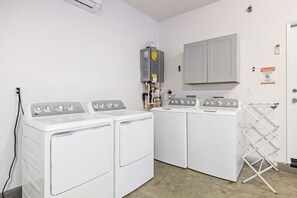 Ein Waschraum mit zwei Waschmaschinen, einem Trockner, einem Warmwasserbereiter und einer weißen Tür mit Handtuchhalter.
