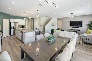 Eine moderne Küche mit Kochinsel, Essbereich mit Stühlen und Wohnzimmer mit Sofa und Fernseher.