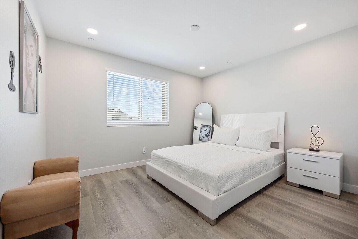 Un dormitorio con cama, mesita de noche, silla y ventana con persianas.