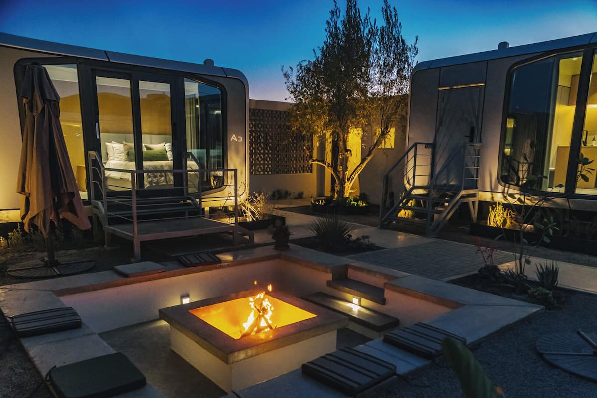 Un espace de vie extérieur moderne doté d’un foyer, de sièges et d’une chambre à coucher fermée par des parois de verre.