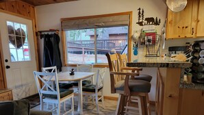 A cozy kitchen with wooden cabinets, a dining area with white chairs, and a large window offering a view of the outside.