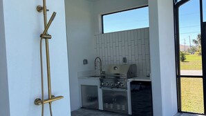 A modern outdoor kitchen with a built-in grill, a ceiling fan, and a showerhead. - Upscale Getaway (Rotonda West)