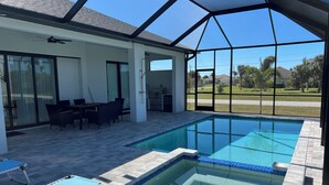A swimming pool with a glass enclosure, a patio area with outdoor furniture, and a view of the neighborhood. - Upscale Getaway (Rotonda West)