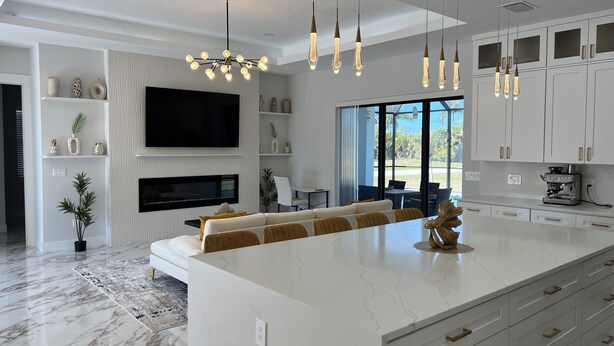 A modern kitchen with a large island, white cabinetry, and a built-in TV. - Upscale Getaway (Rotonda West)