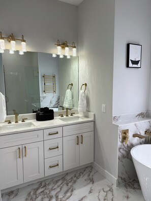 A modern bathroom with a large mirror, dual sinks, and a bathtub. - Upscale Getaway (Rotonda West)