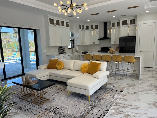 A modern kitchen with white cabinets, a black range hood, and a bar area with gold chairs. - Upscale Getaway (Rotonda West)