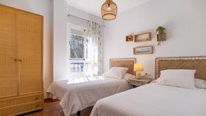 Une chambre avec deux lits, une armoire, une fenêtre avec des rideaux, une table de chevet avec une lampe et des étagères murales décoratives.