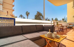 A modern outdoor seating area with a sofa, a small table with a teapot and cups, and a view of palm trees and buildings in the background. - Nice apartment in Torrox with swimming pool (Torrox)