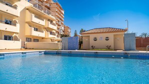 Une piscine dont le bord est recouvert de carrelage, entourée d’un bâtiment doté de balcons et surmonté d’un toit en tuiles.