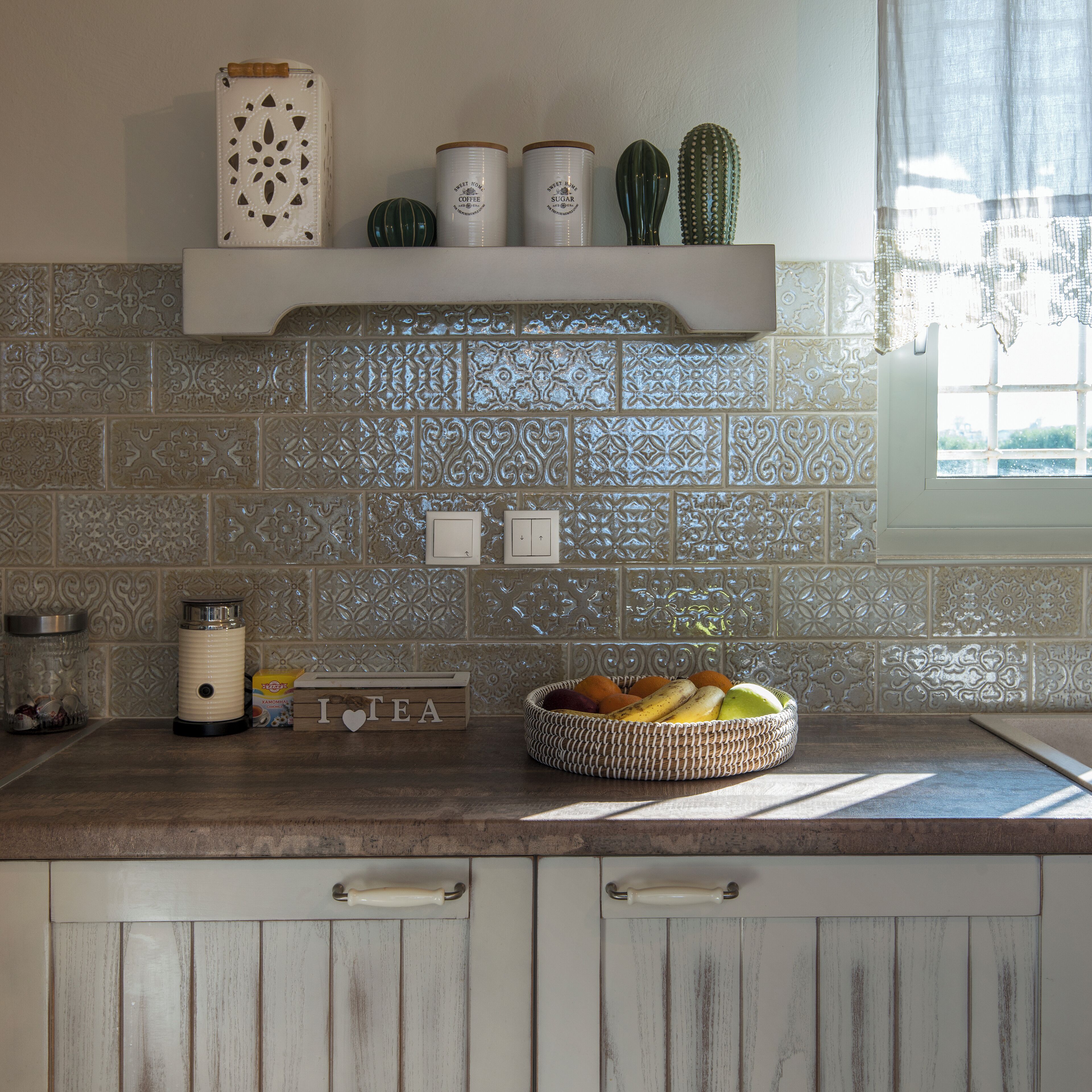 Una cuina amb un mosaic decoratiu a la paret, un cesto de fruita al taulell, i un cartell que diu 'I ♥ TEA'.