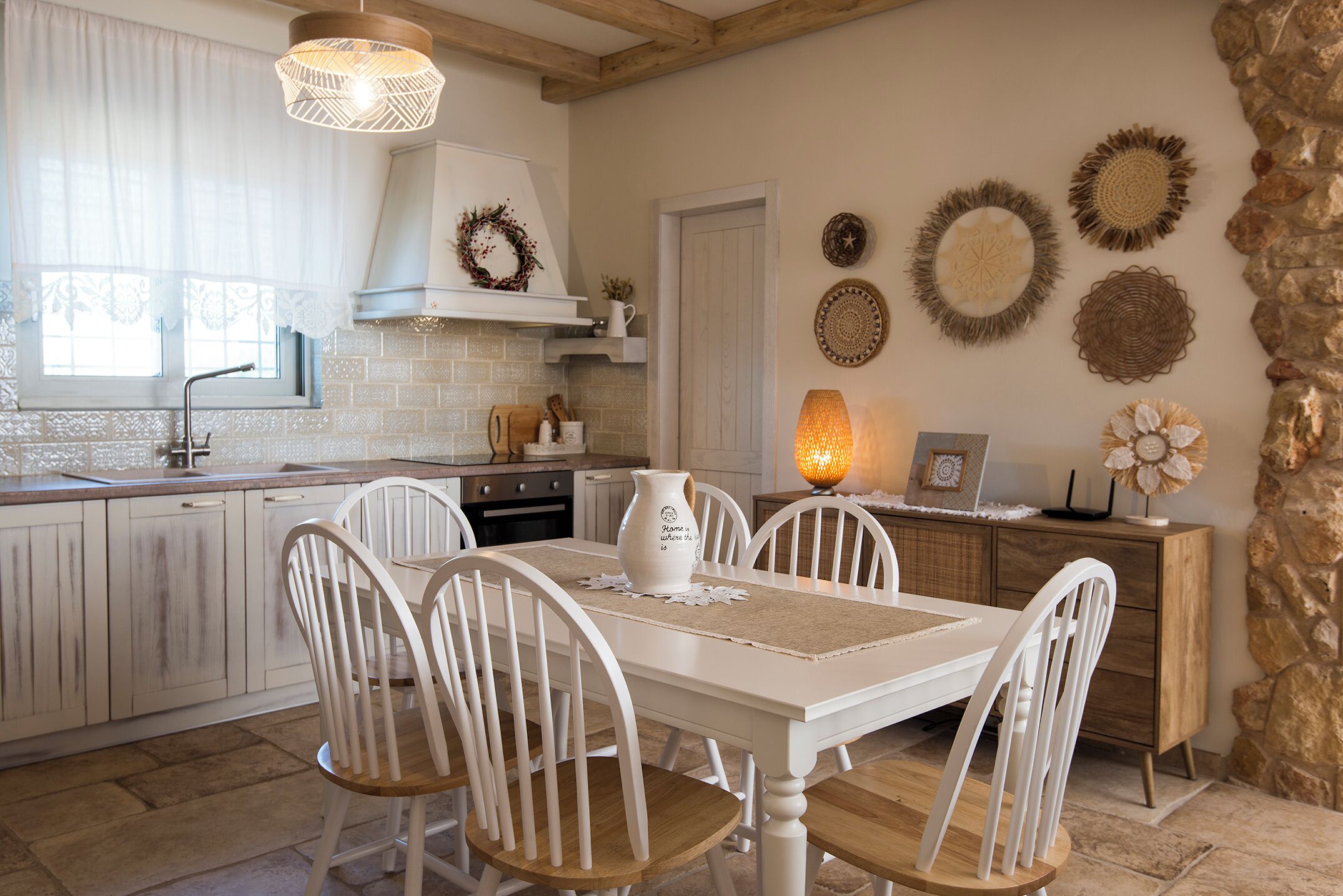 A kitchen with white cabinetry, a wooden dining table with four chairs, a hanging light fixture, and decorative wall art.