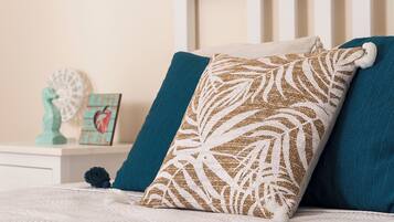 Un lit bien fait, recouvert d’une couette blanche, agrémenté de coussins turquoise et d’un coussin décoratif orné d’un motif de feuilles.