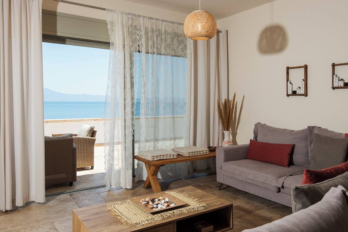 Un salon avec vue sur la mer, un canapé, une table basse agrémentée d’objets décoratifs et un fauteuil en osier.