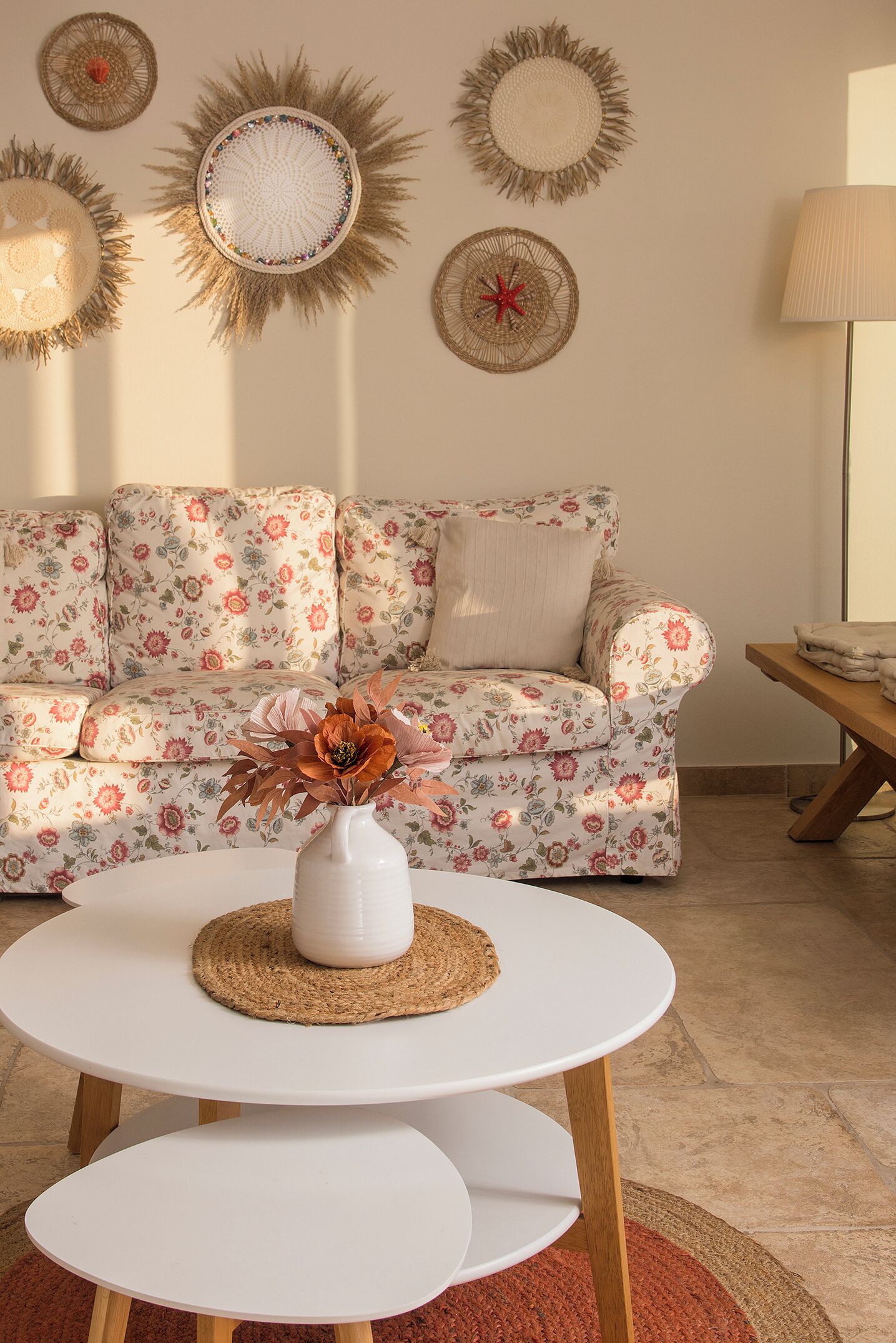 A living room with a floral sofa, a white coffee table with a woven placemat, and decorative wall art.