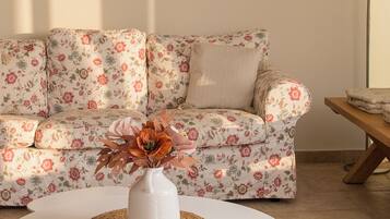 A living room with a floral sofa, a white coffee table with a woven placemat, and decorative wall art.
